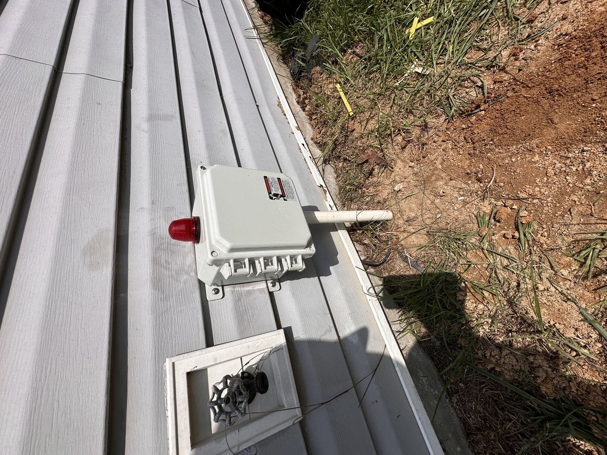 Exterior septic alarm panel with red warning light on home siding